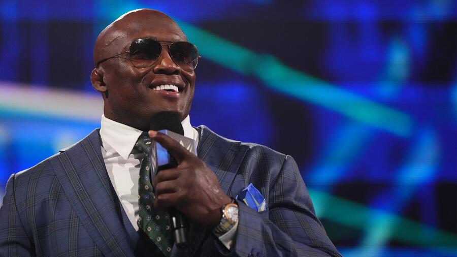 Bobby Lashley in a tailored suit and sunglasses holding a microphone during a WWE SmackDown broadcast