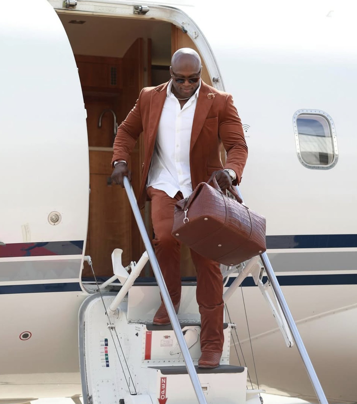 Bobby Lashley in a tailored suit descending the stairs of a private jet